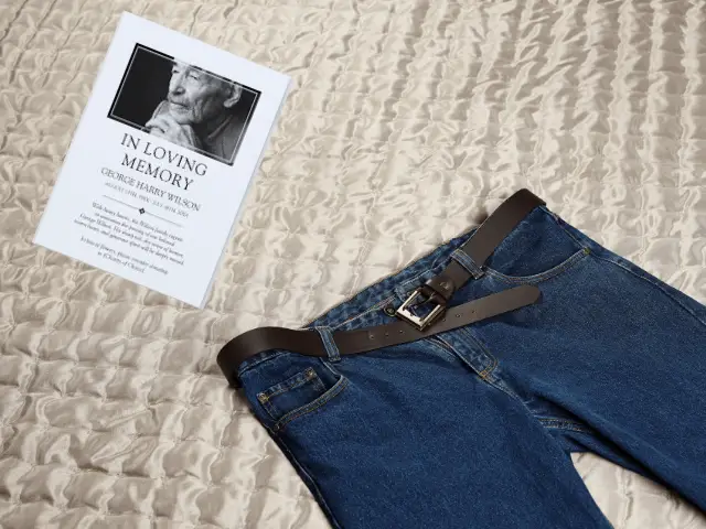 Jeans on a bed next to funeral program