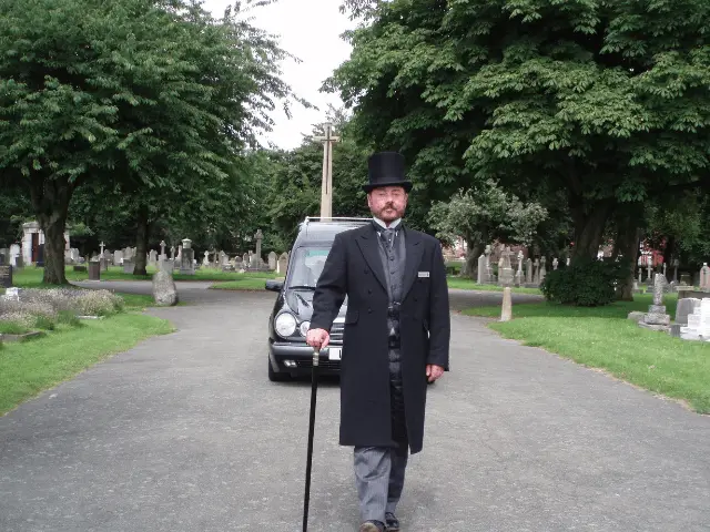 funeral director walking in front of a hearse
